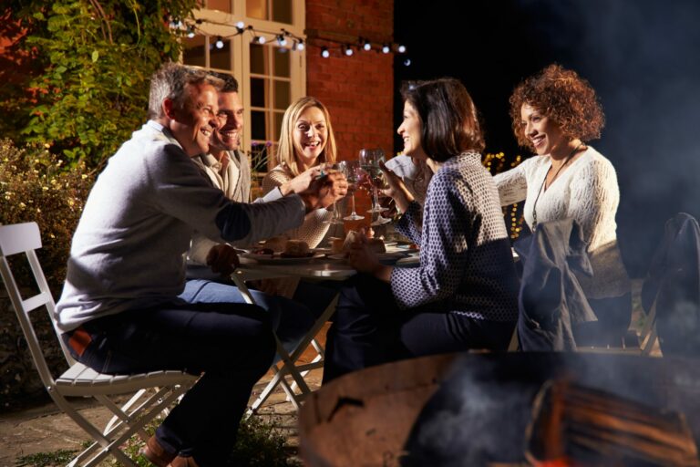 Mature Friends Enjoying Outdoor Evening Meal Around Firepit