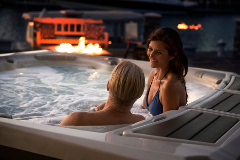 Man and woman enjoying hydrotherapy in a hot tub by the fire.