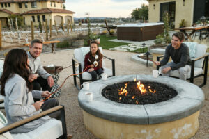 Family sitting by the fire with a hot tub and hammock in the background