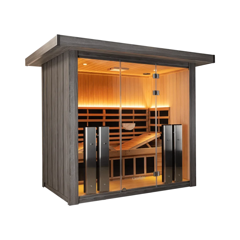 Exterior view of a dark-stained wooden sauna cabin with glass doors, warm interior lighting visible through the glass panels.