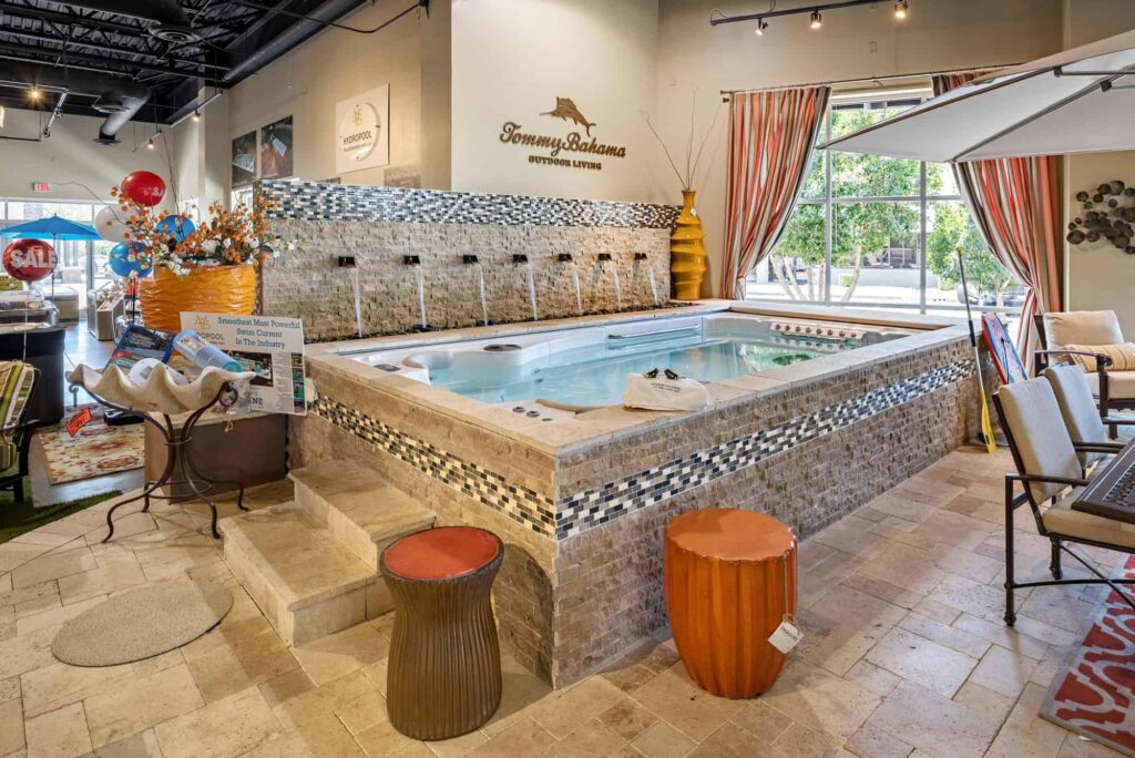 Indoor showroom with a long stone water feature, striped curtains, and orange ceramic stools; sale balloons on the left corner.