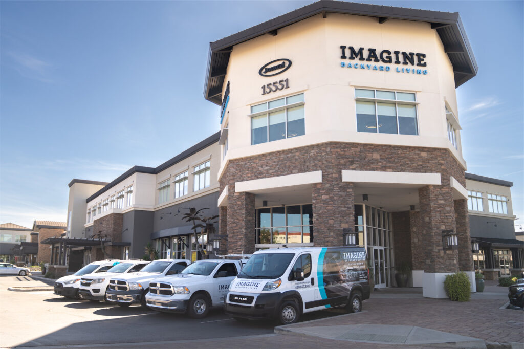 Commercial building with 'IMAGINE BACKYARD LIVING' sign and fleet of Imagine vans in parking lot