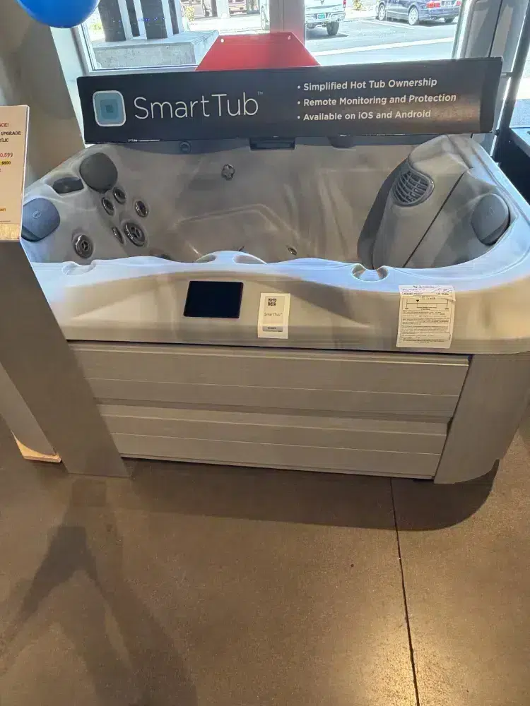 Showroom SmartTub hot tub with built‑in controls and a feature banner in the background on the display stand.