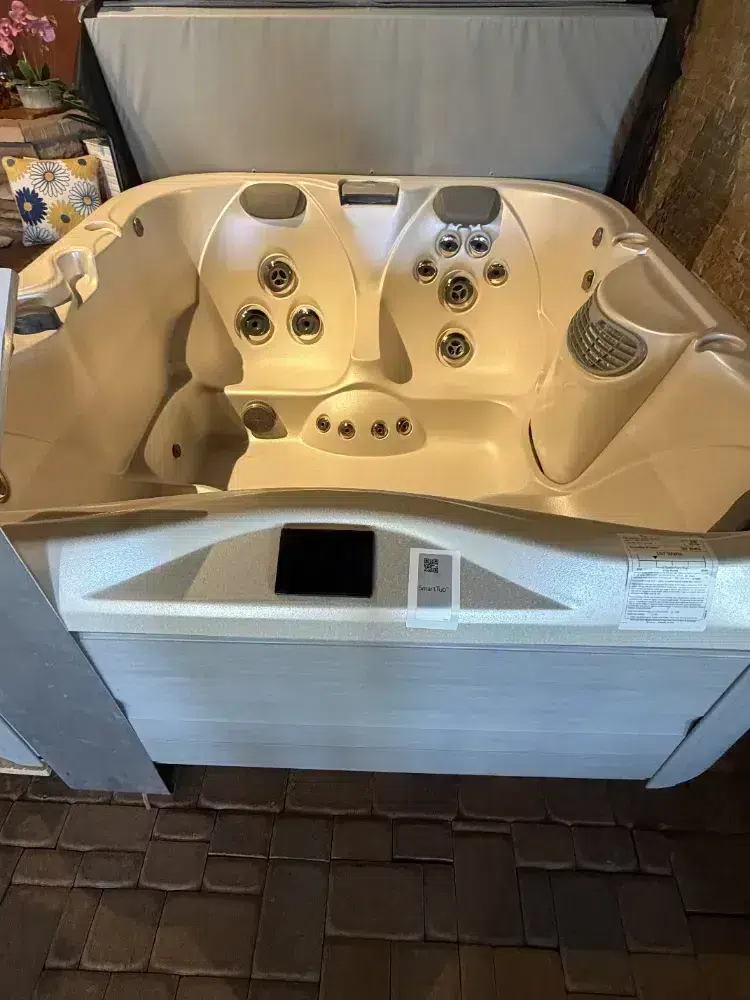 White four-person hot tub with multiple jets and built-in headrests, indoor setting.