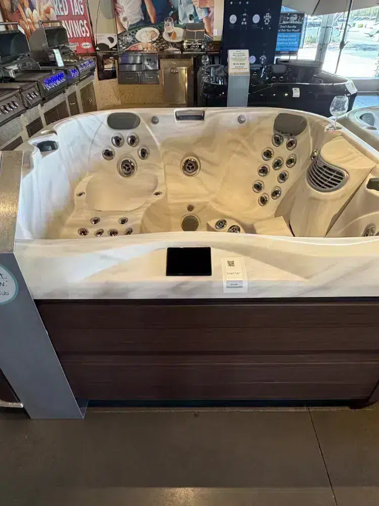 White hot tub showroom display with multiple massage jets and built-in headrests, edge counter with a phone nearby.