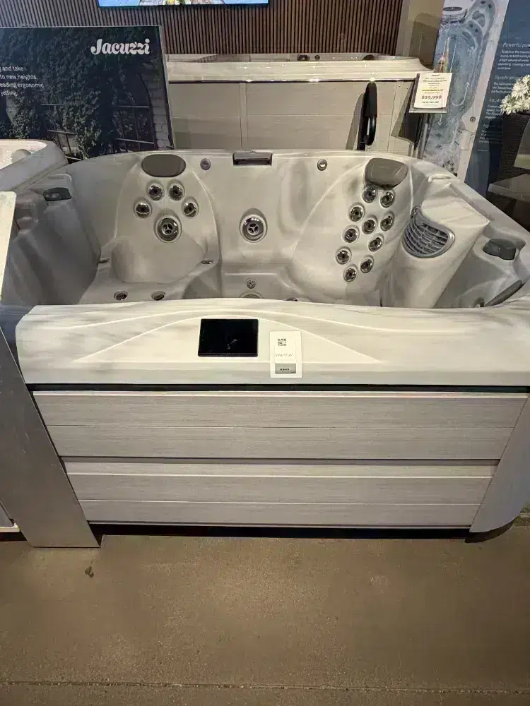 Gray showroom hot tub with multiple jets and a built-in control panel on a display pedestal.