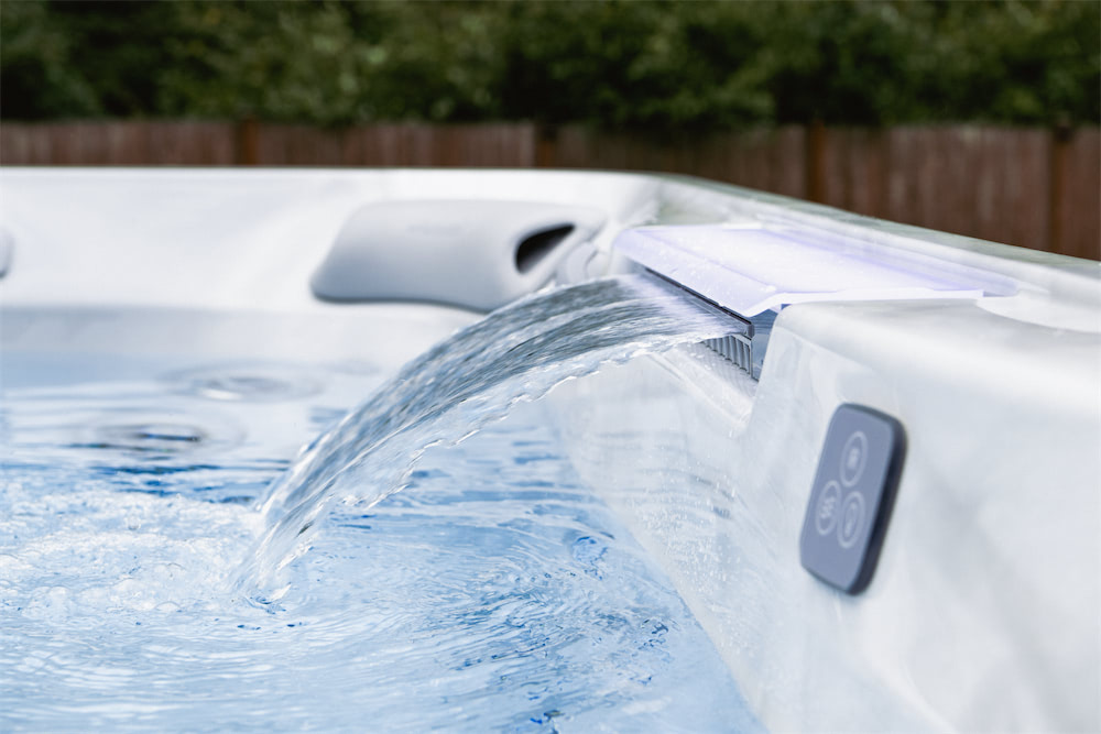 Hot tub with water cascading from a spout into the pool; control panel on the side.