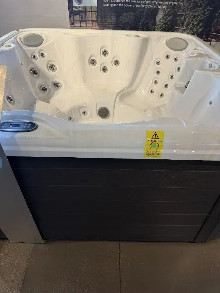 White rectangular hot tub with multiple massage jets and a built-in control panel, displayed in a showroom.
