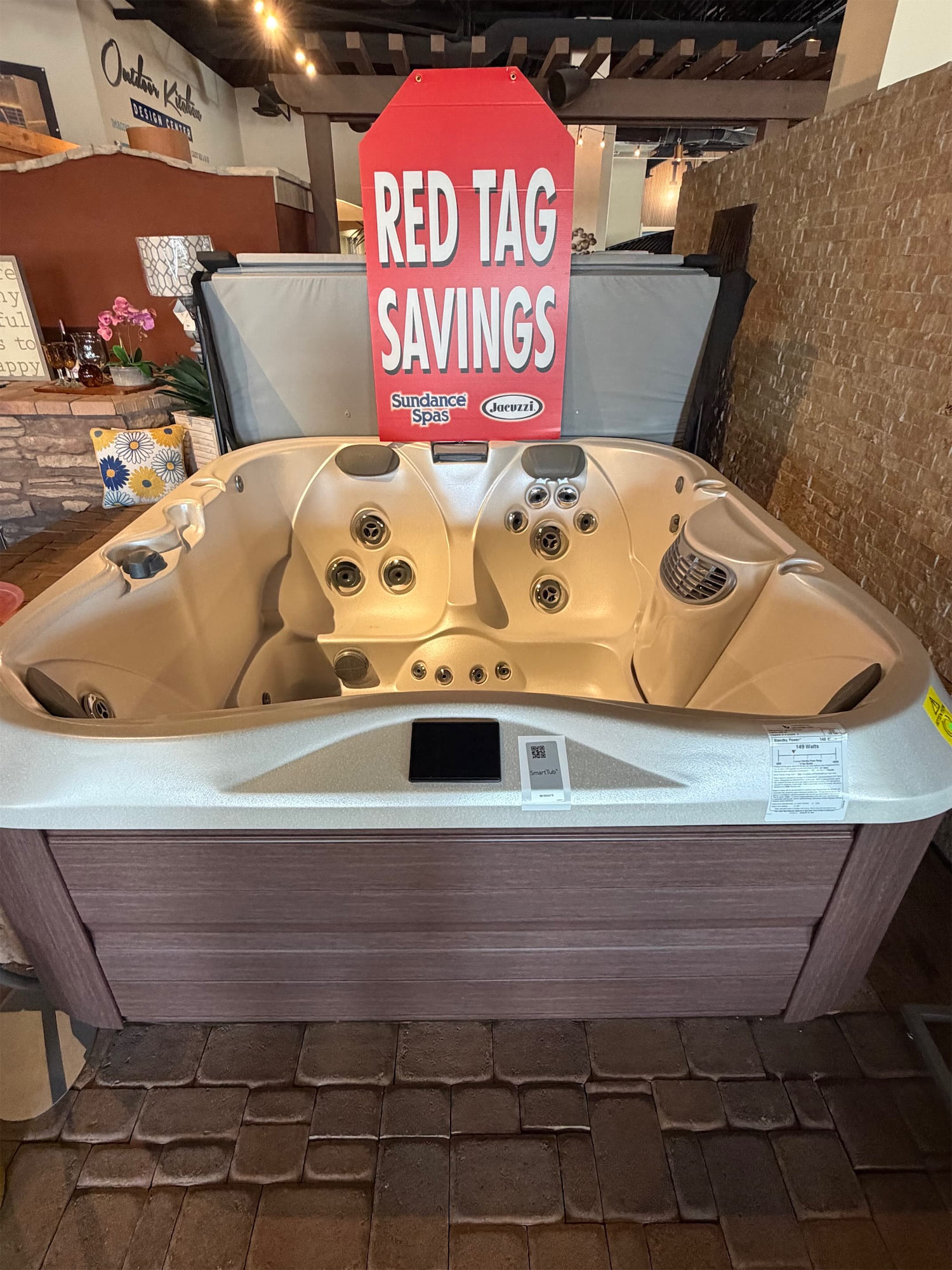 Red Tag Savings banner attached to a beige hot tub in a showroom with brand logos visible (Sundance Spas, Jacuzzi).
